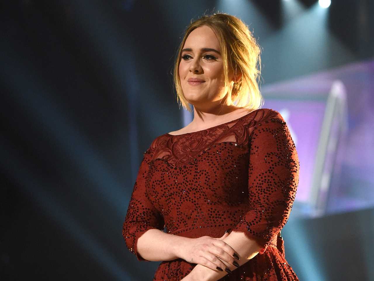 Adele in a red long sleeve gown holding a microphone on stage.