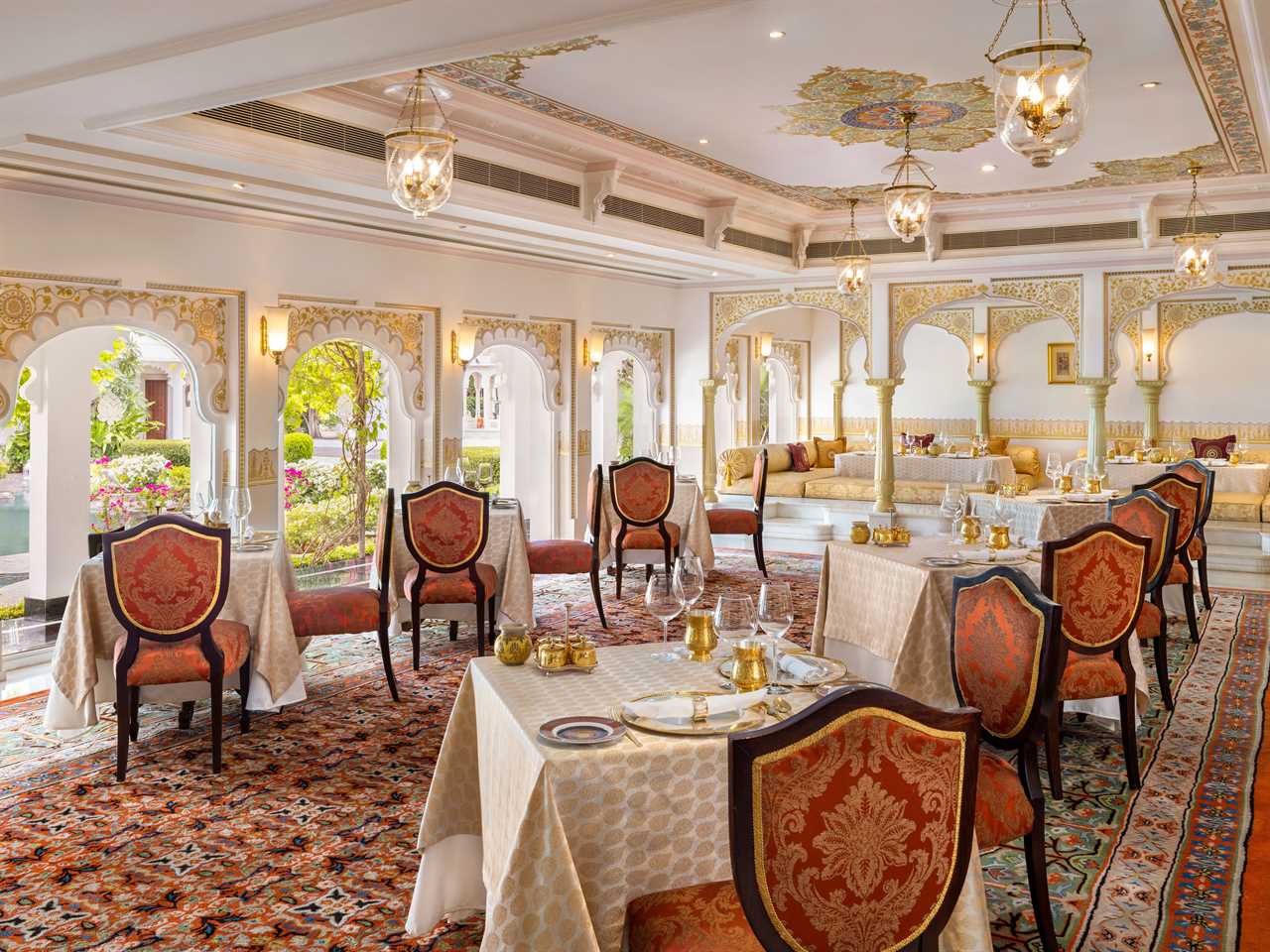 A restaurant with square tables, red and gold chairs, and beautiful architecture.