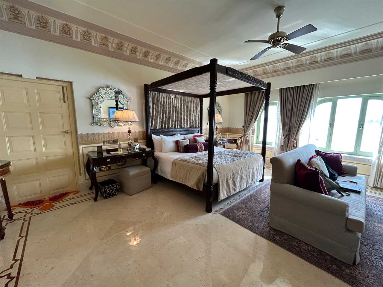 A hotel room with a large canopy bed, large windows, and a couch.