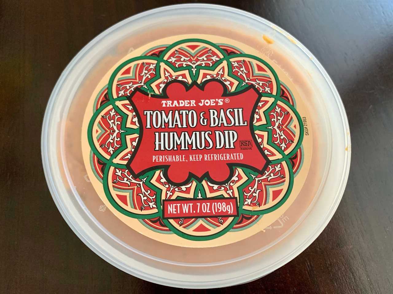 red and clear tub of trader joe's tomato basil hummus on wood table