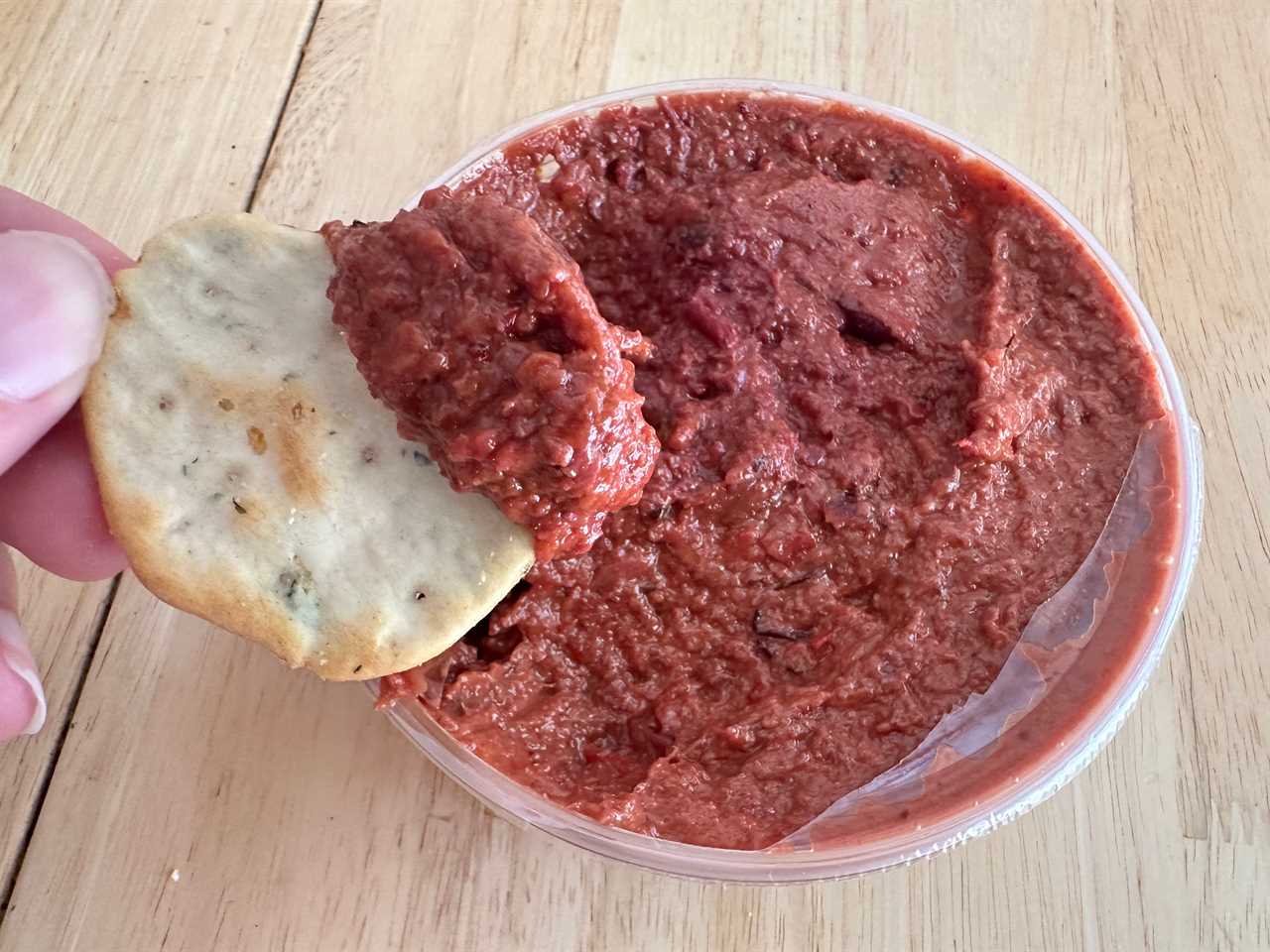 Hand dipping cracker into red Trader Joe's cranberry and red pepper dip