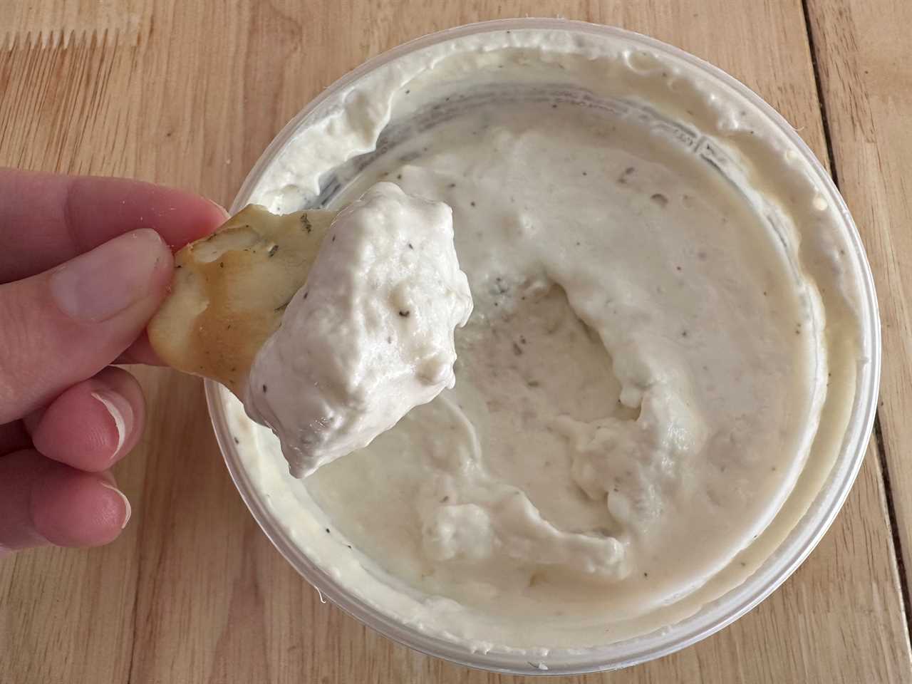 Hand dipping chip in white-ish cauliflower and jalapeno dip from Trader Joe's