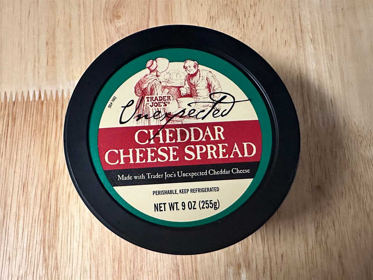 beige, red, and green tub of Trader JOe's unexpected cheddar dip on wood table