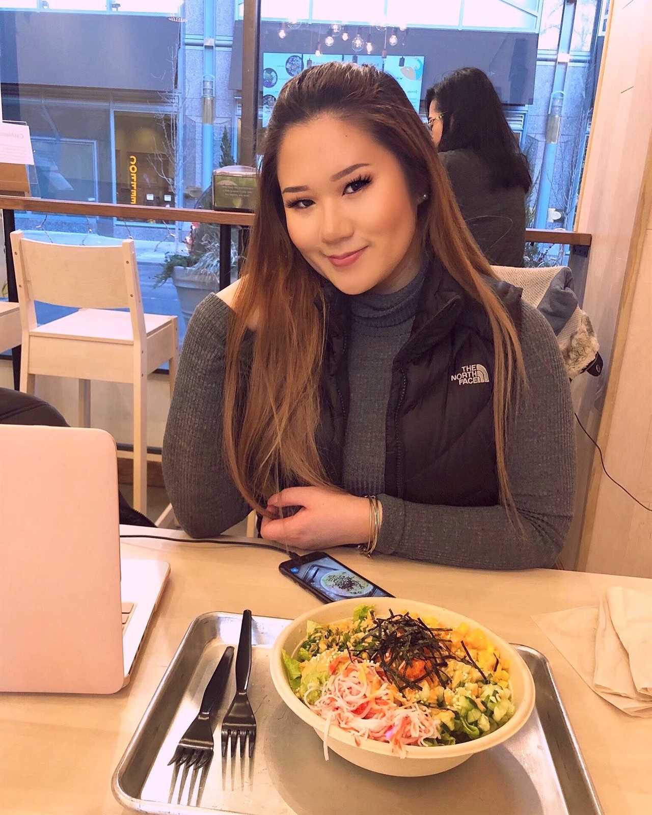 Kelsey Lam sitting at a table in a food venue. There is a tray with a salad on it in front of her.