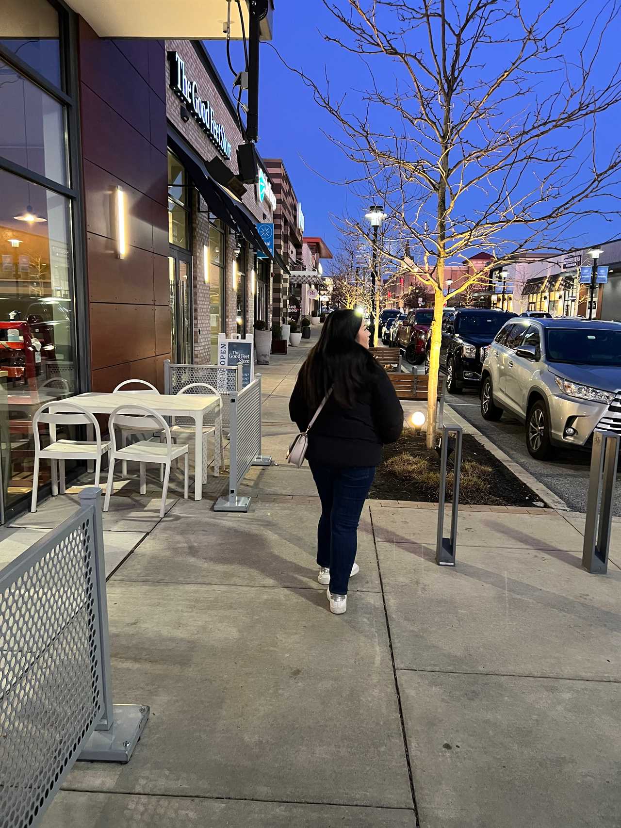 Kelsey Lam walking down a street in the suburbs. There is a store to her right and parked cars to her left.