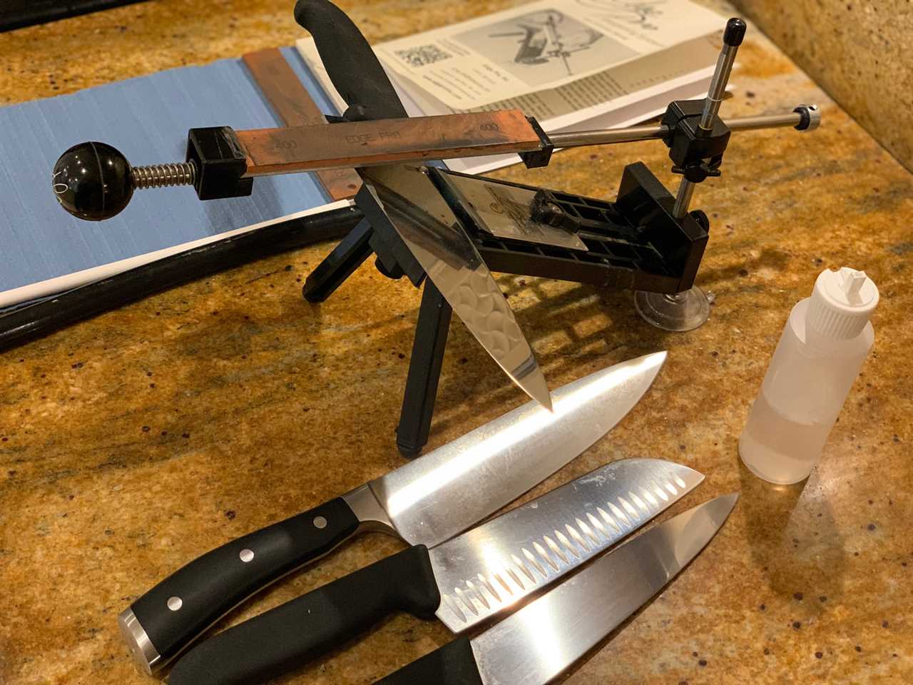 The Edge Pro Apex 2 sharpening a chef’s knife with three other knives on a granite countertop.