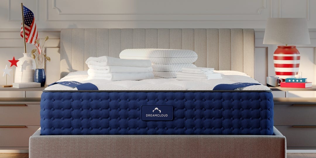 a dreamcloud mattress on a grey bed frame with folded sheets and pillows on top and americana decorations on the bedside tables