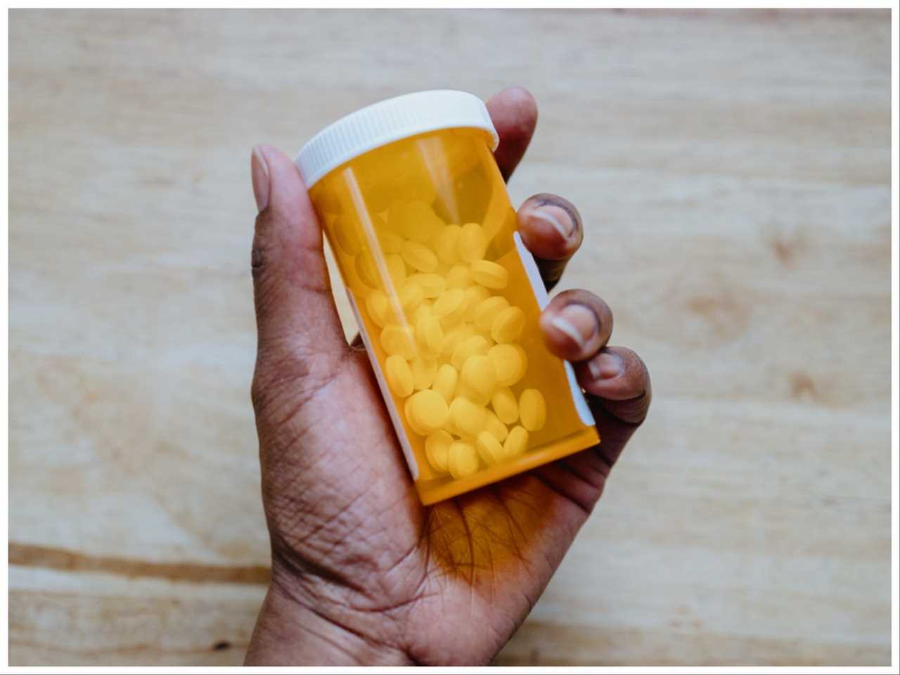 A black woman's hand holds a prescription bottle of drug tablets