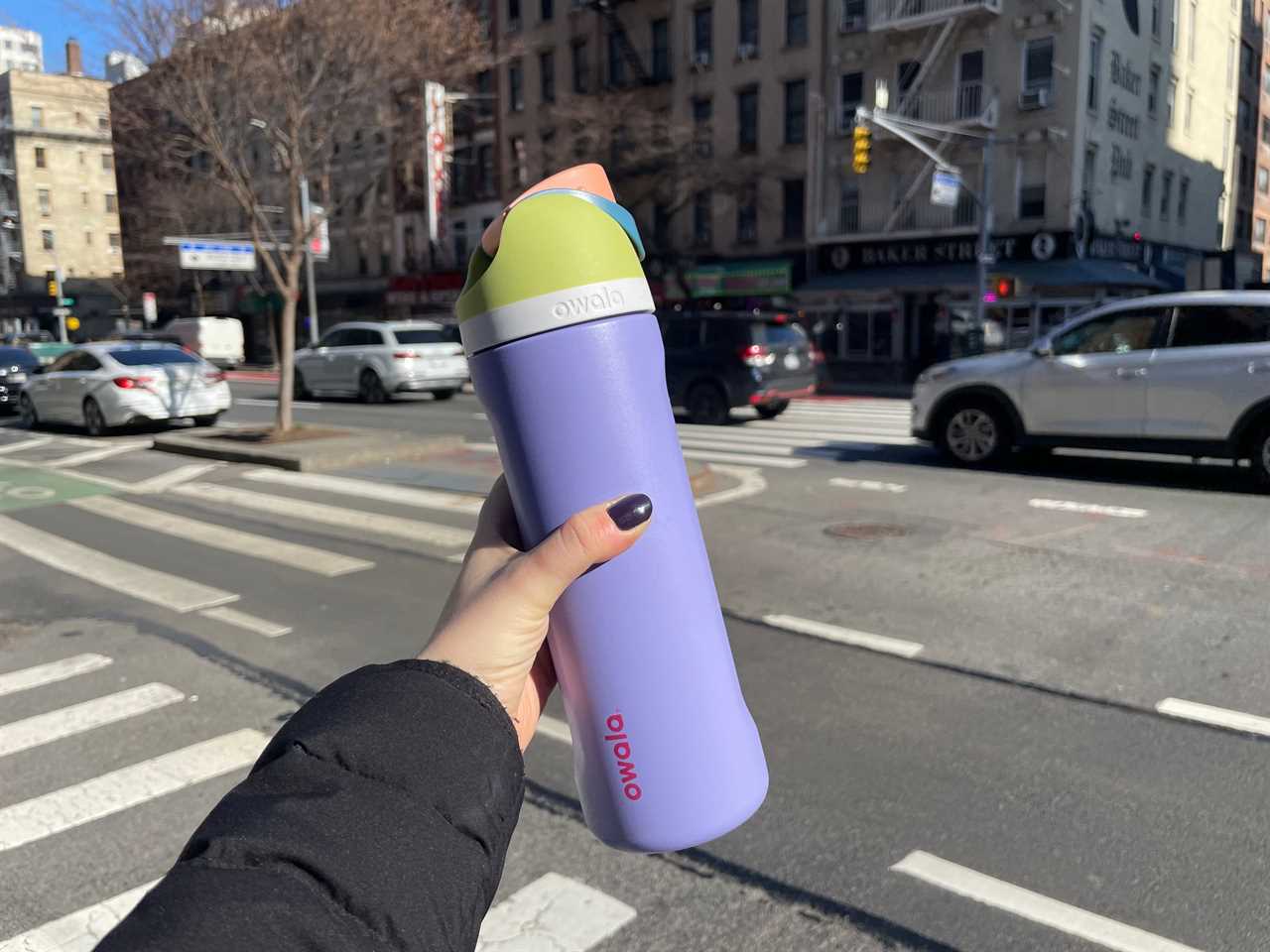 A hand holding the Owala FreeSip bottle in front of a New York City street.