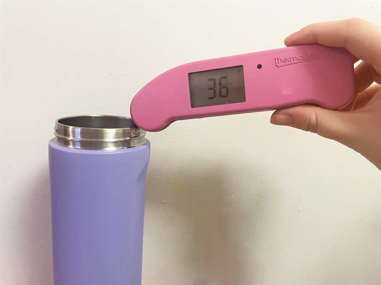 A hand holding a pink meat thermometer measuring the water temperature inside an Owala water bottle.