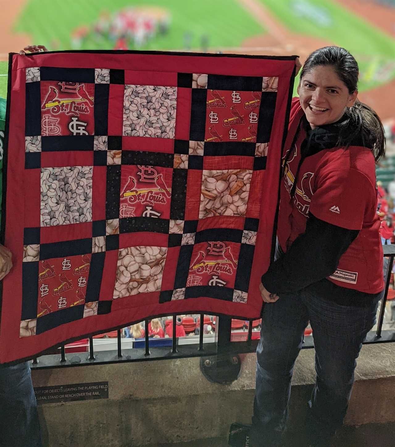 A woman holding a red St. Louis Cardinals quilt at a baseball game.