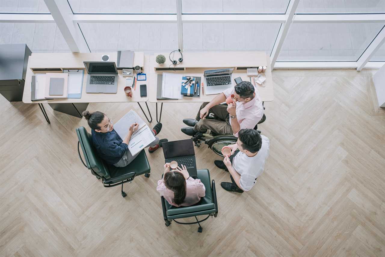 Arial photo of four employees sitting in green chairs around one long desk