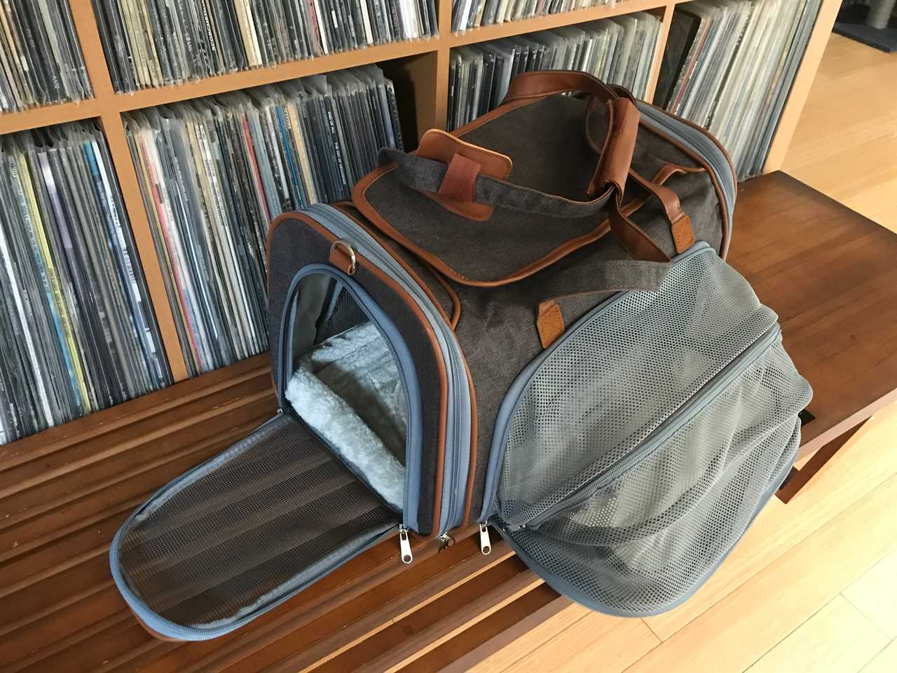 A gray expandable pet carrier with mesh door is shown fully expanded on a bench.