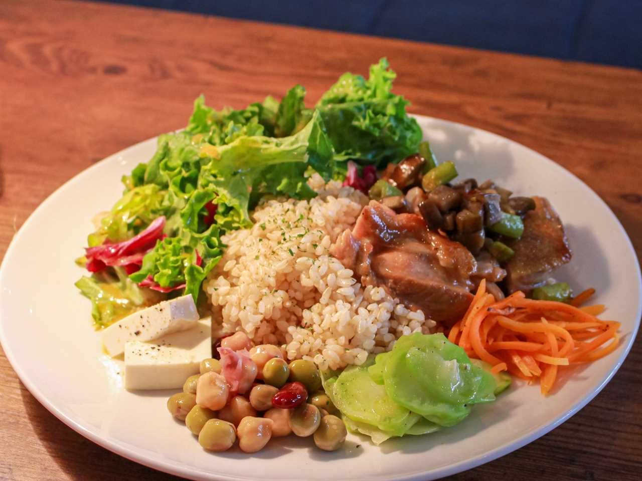 A white plate with rice, beans, salad, cheese, and sautéed chicken.