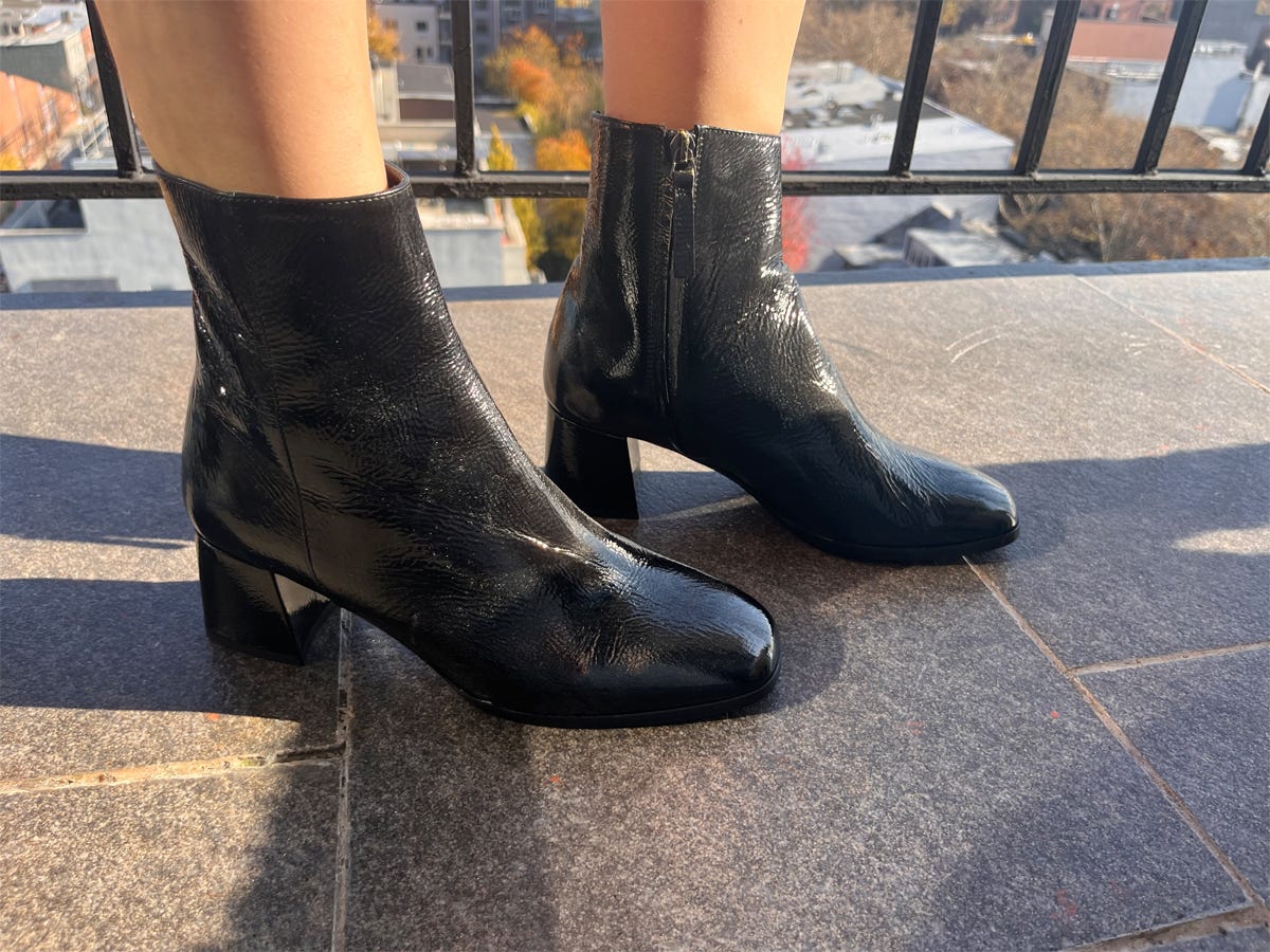 Person's feet shown wearing M. Gemi The Christina ankle boots while standing on a balcony.