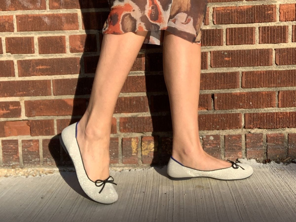 Silver Rothy's ballet flats on model against a brick wall background.