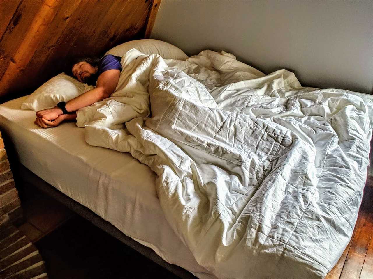 The author pretends to sleep while covered by the Brooklinen Weighted Comforter in bed.