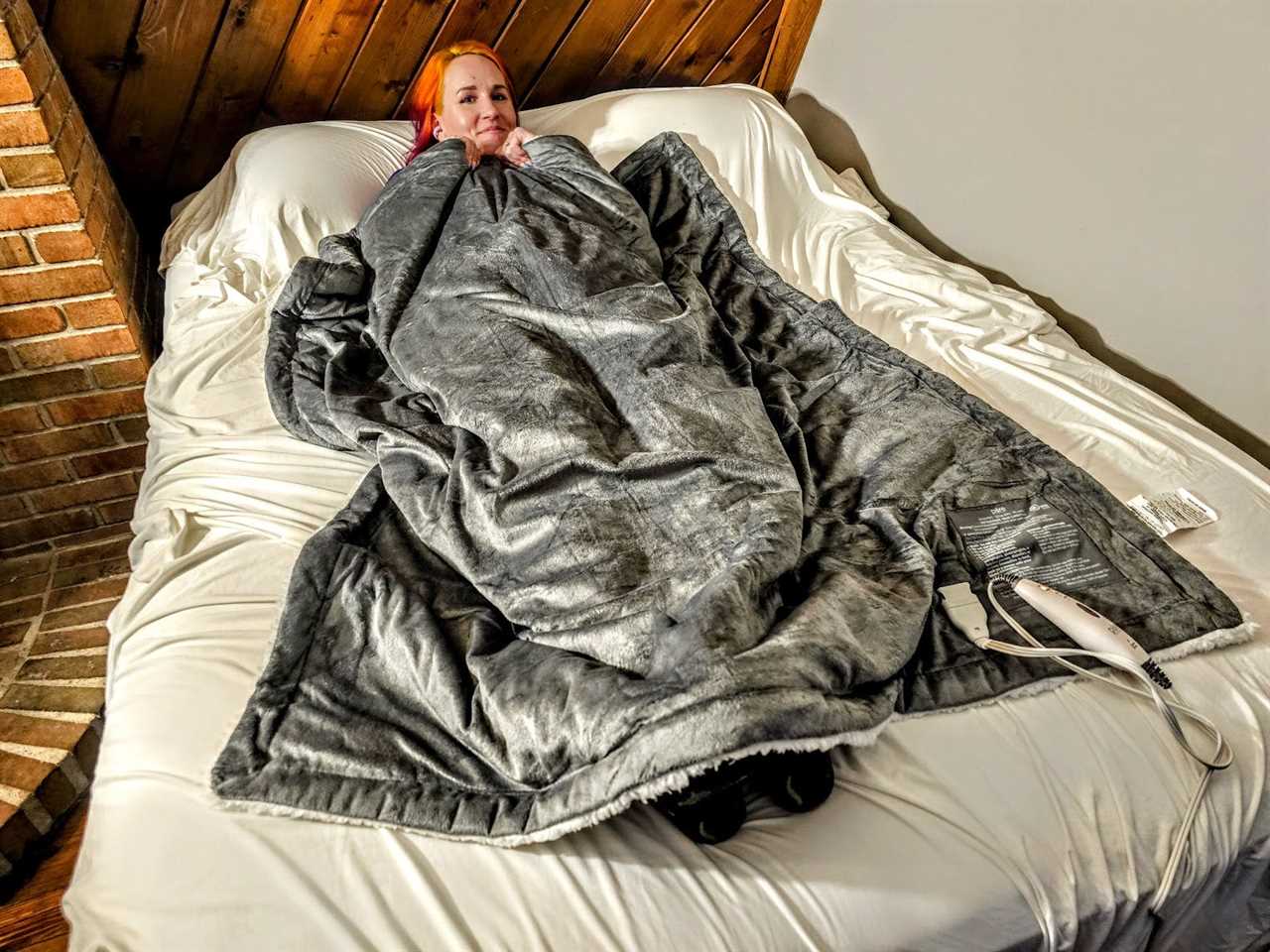 A woman smiles while lounging under the Pure Enrichment WeightedWarmth weighted blanket on a bed