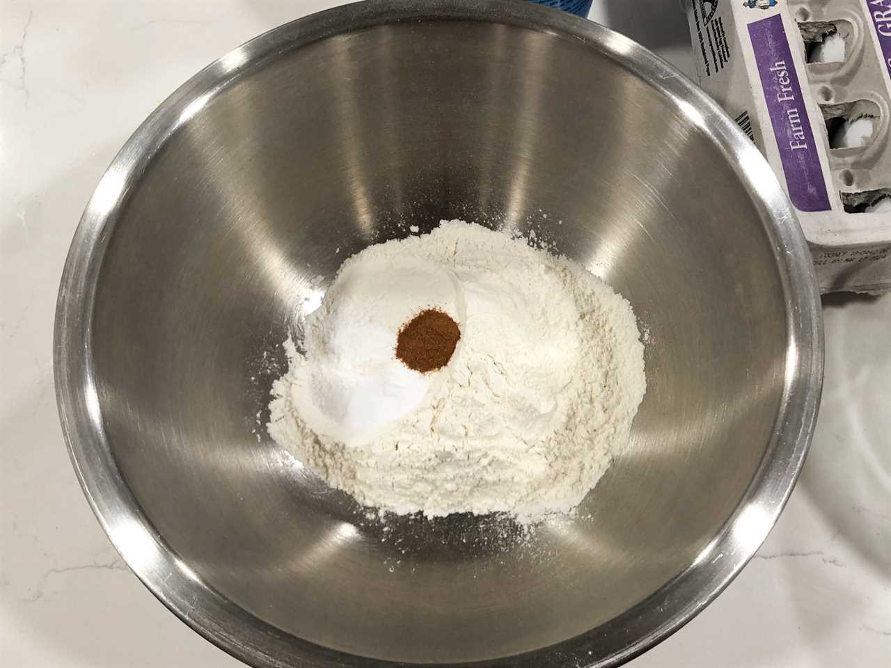 Dry ingredients in a stainless-steel bowl, and a carton of eggs in the background.