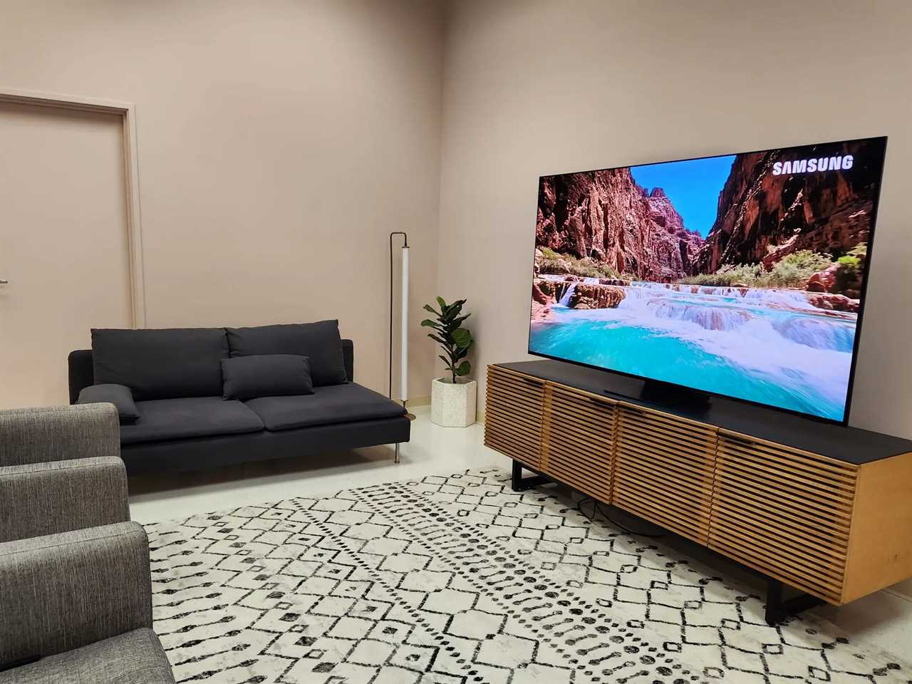 A Samsung S95C 4K TV on a TV stand in a living room displaying a scene featuring a river and mountains.