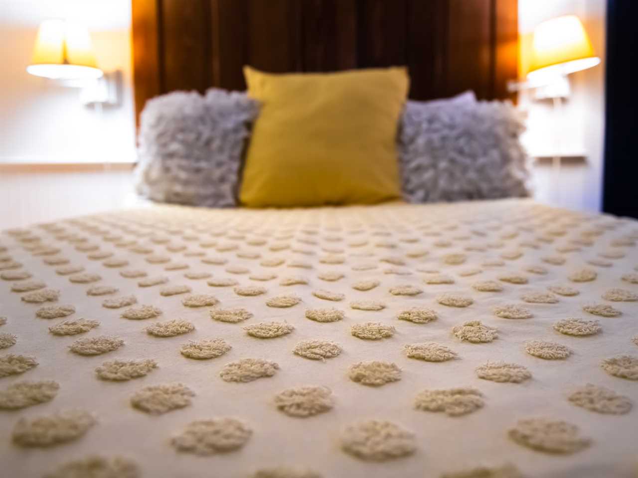 bed with a textured polka-dot bedspread and yellow and purple throw pillows