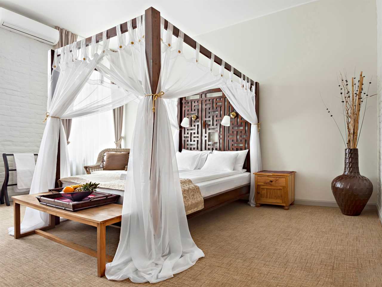 clean, neutral bedroom with a large wooden canopy bed with sheer white drapes