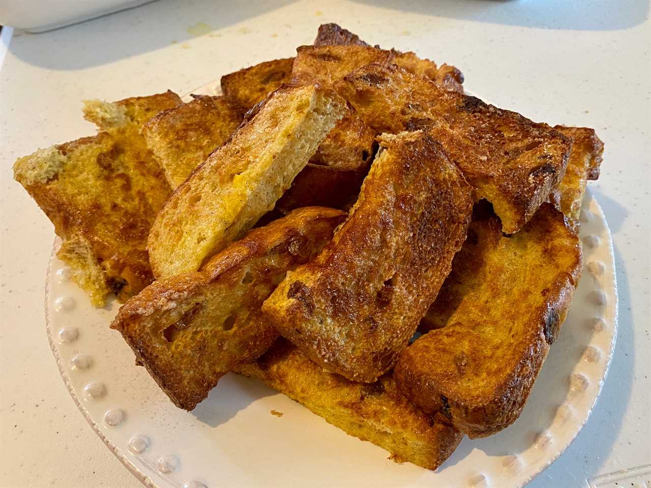 air fryer french toast sticks stacked on white plate