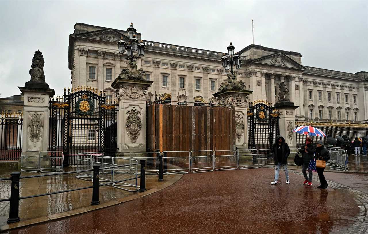 People walk past a set of boarded up gates to Buckingham Palace in London on March 10, 2024.