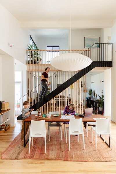 The main living area is on the second floor in an open double-height space where the ceiling peaks at 15 feet under an angled roof. It contains an airy kitchen/dining area and a living room. A hallway leads to the primary bedroom, and a loft contains a bedroom for their kids. The ground floor has an apartment they rent to local teachers.