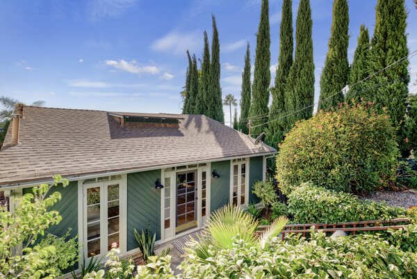 Thick vegetation encloses the sage-green home, allowing it to merge with its surroundings.