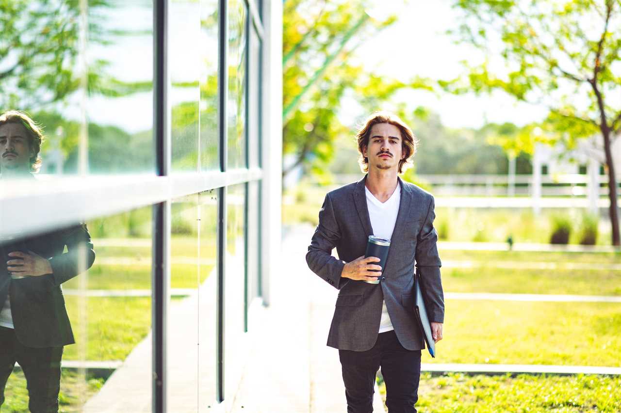 Gen Z guy in front of mirror office building wearing a suit, headed to work or for an interview.