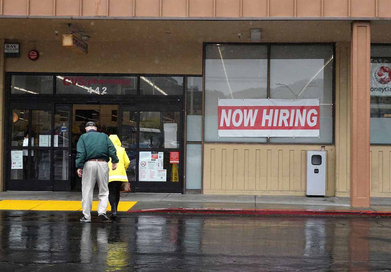 People walk by a now hiring sign posted in front of a CVS store