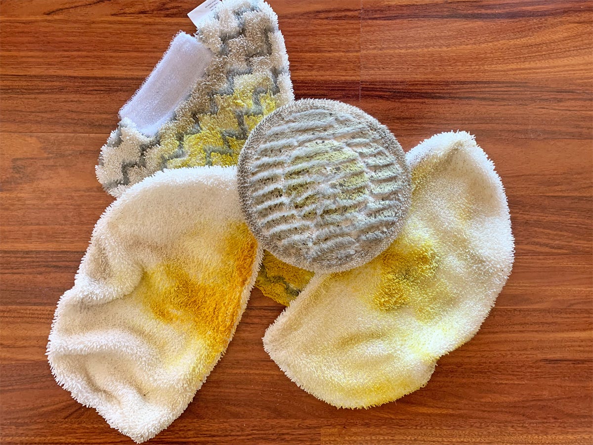 A pile of steam mop cleaning cloths covered in mustard lie on a wooden floor, showing the methodology for testing.