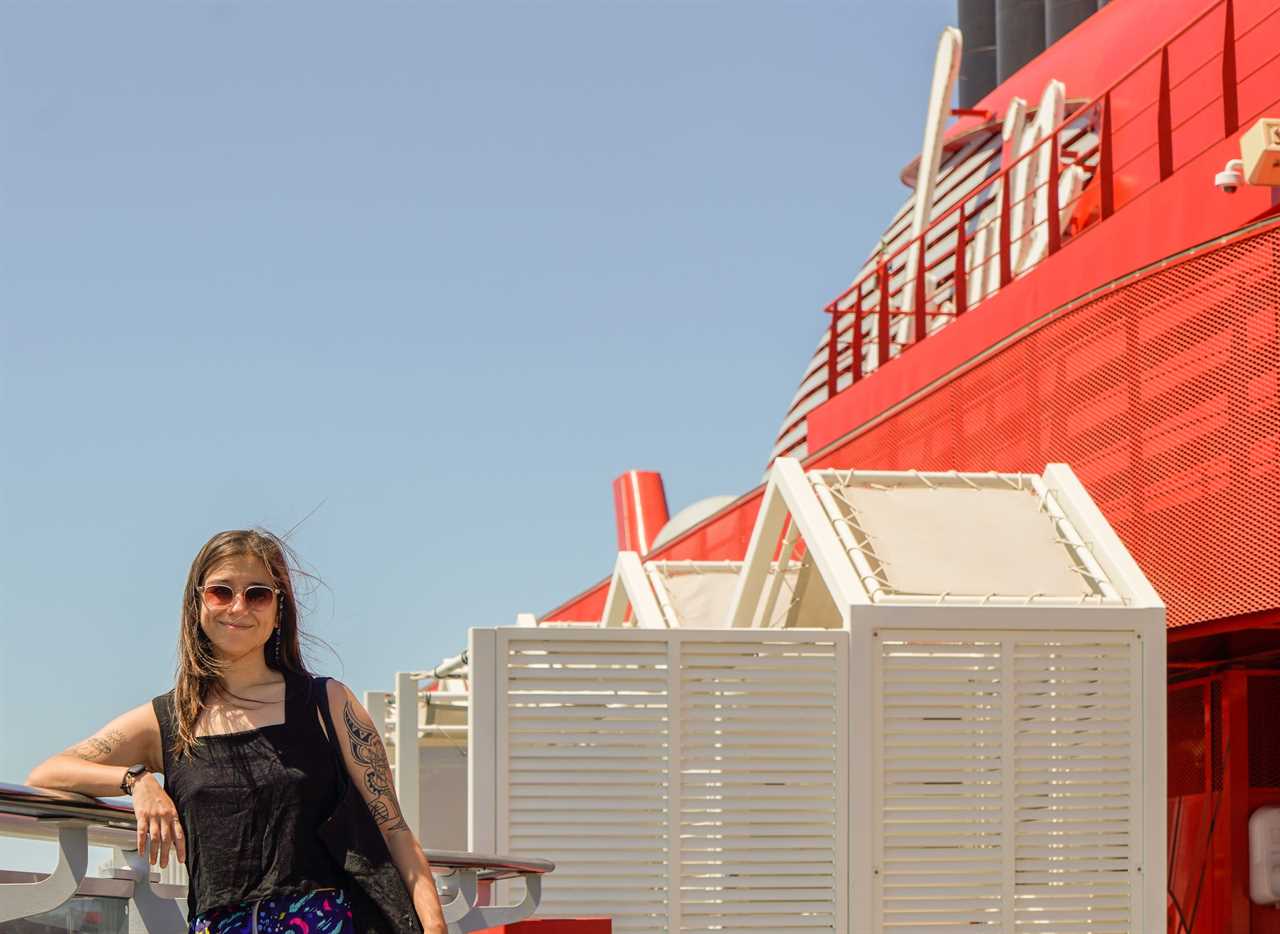 The author leans against the side of a cruise ship with blue skies behind her.