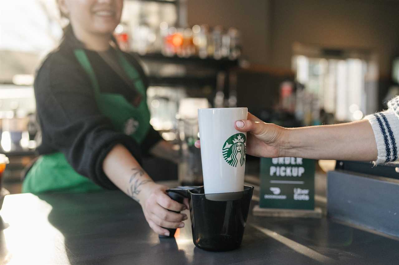 A Starbucks barista handing off a reusable cup drink