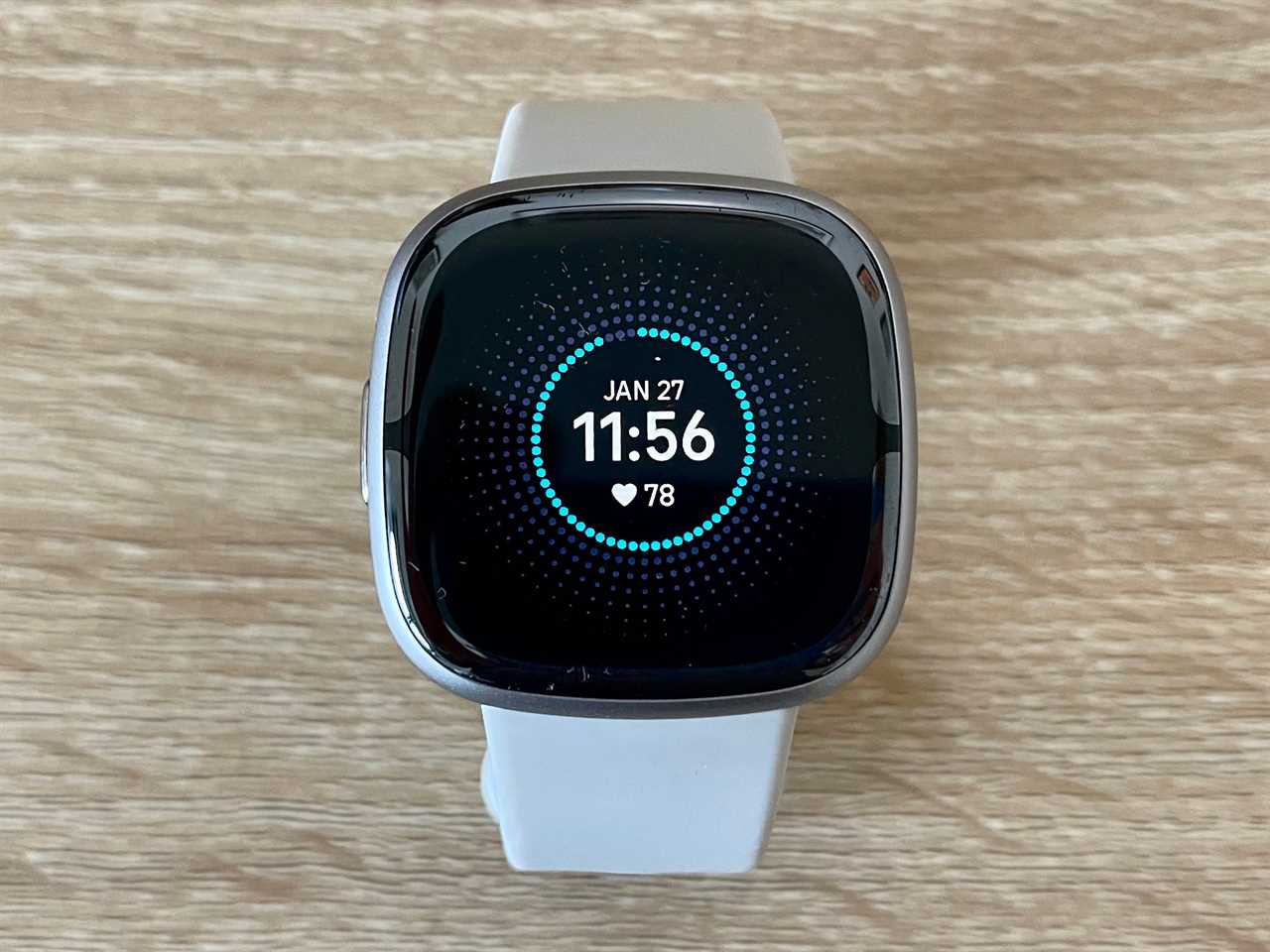 The Fitbit Sense 2 sitting on a wood desk.