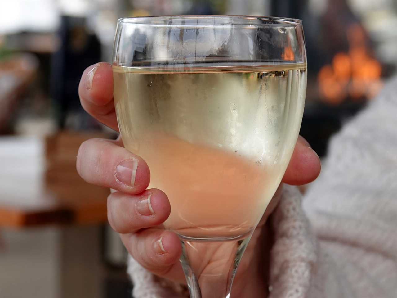 hand holding a glass of chilled white wine over a wooden table