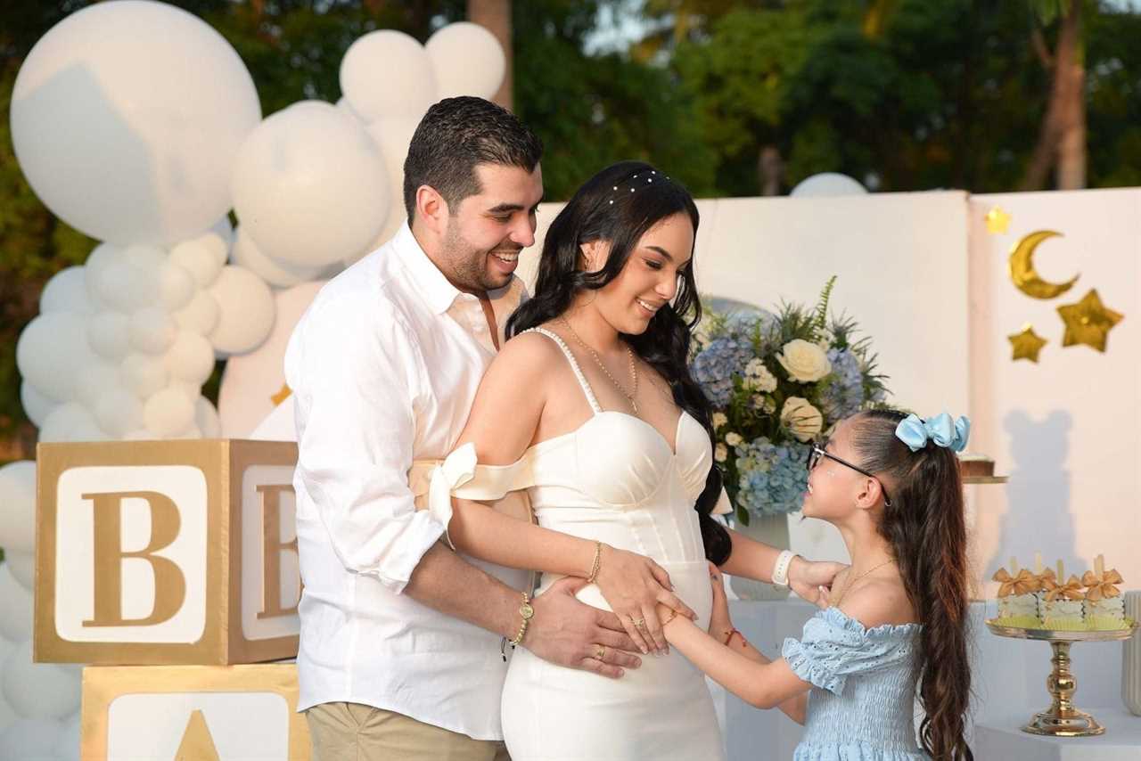 A young girl and her mother's stomach with the father also holding the mother's stomach.