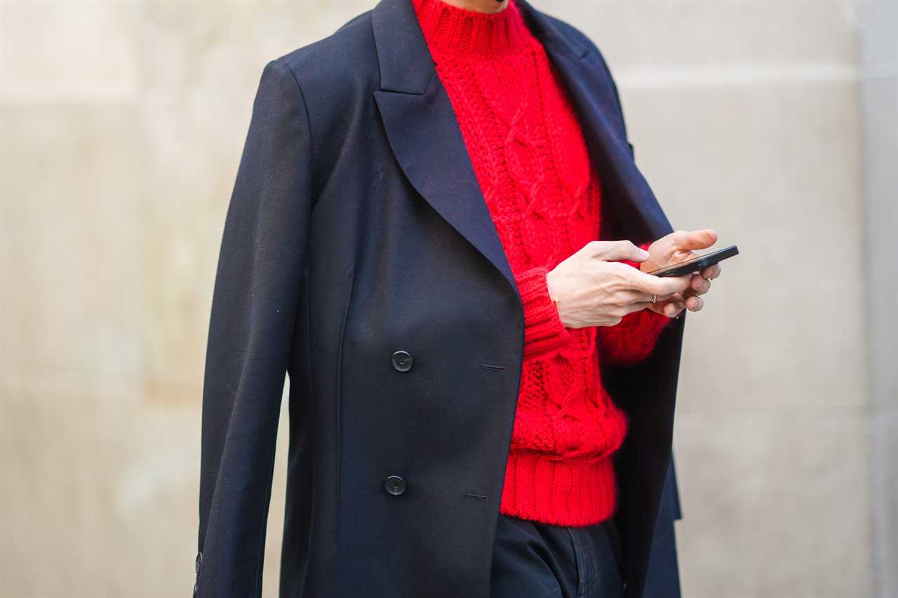 Person texting with red sweater and coat draped over shoulders