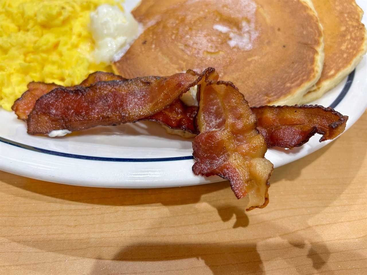 Plate of scrambled eggs, pancakes, and bacon hanging off the plate in the foreground