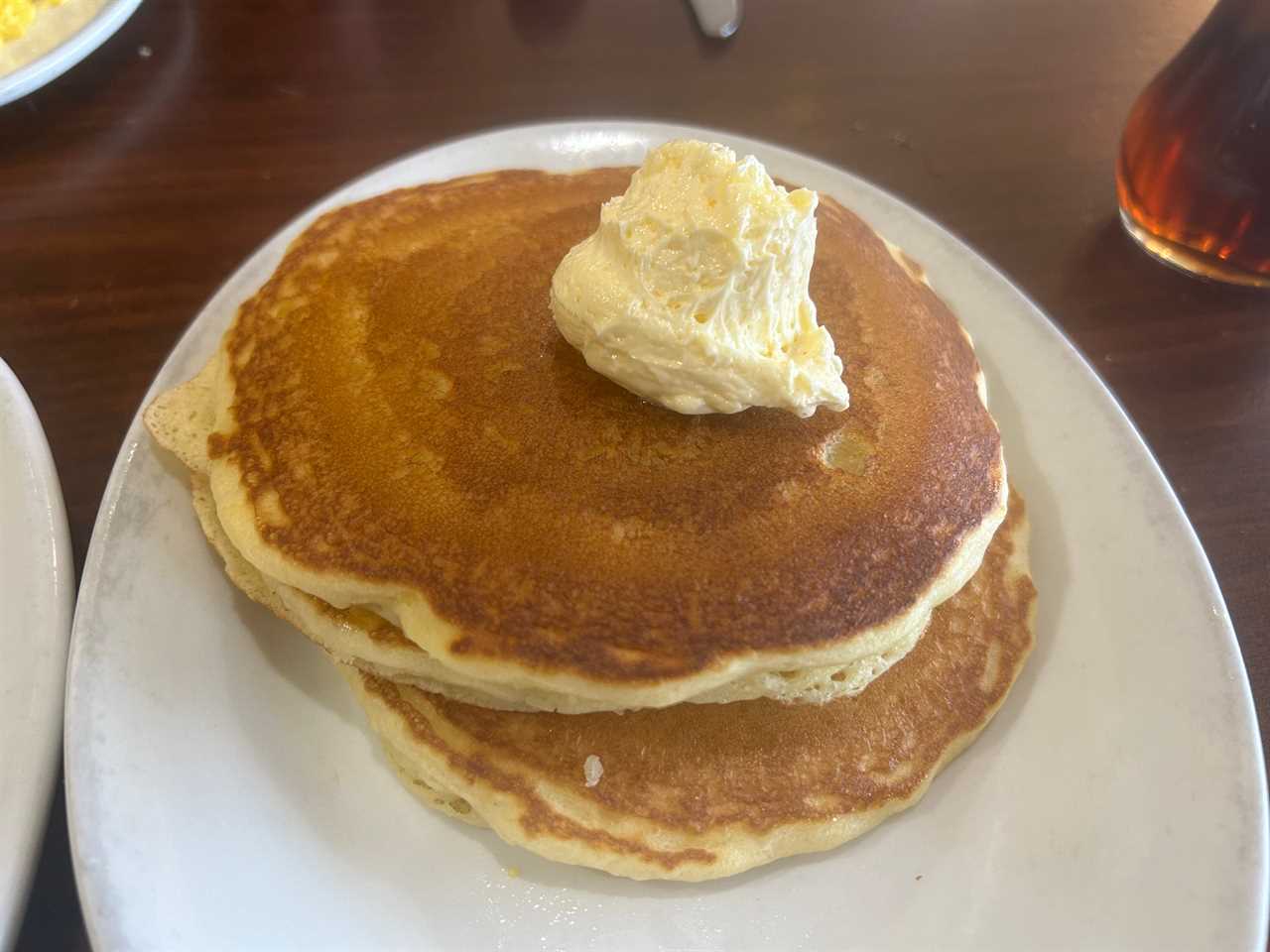Stack of two pancakes on a white plate. A large scoop of butter sits on top of the pancakes