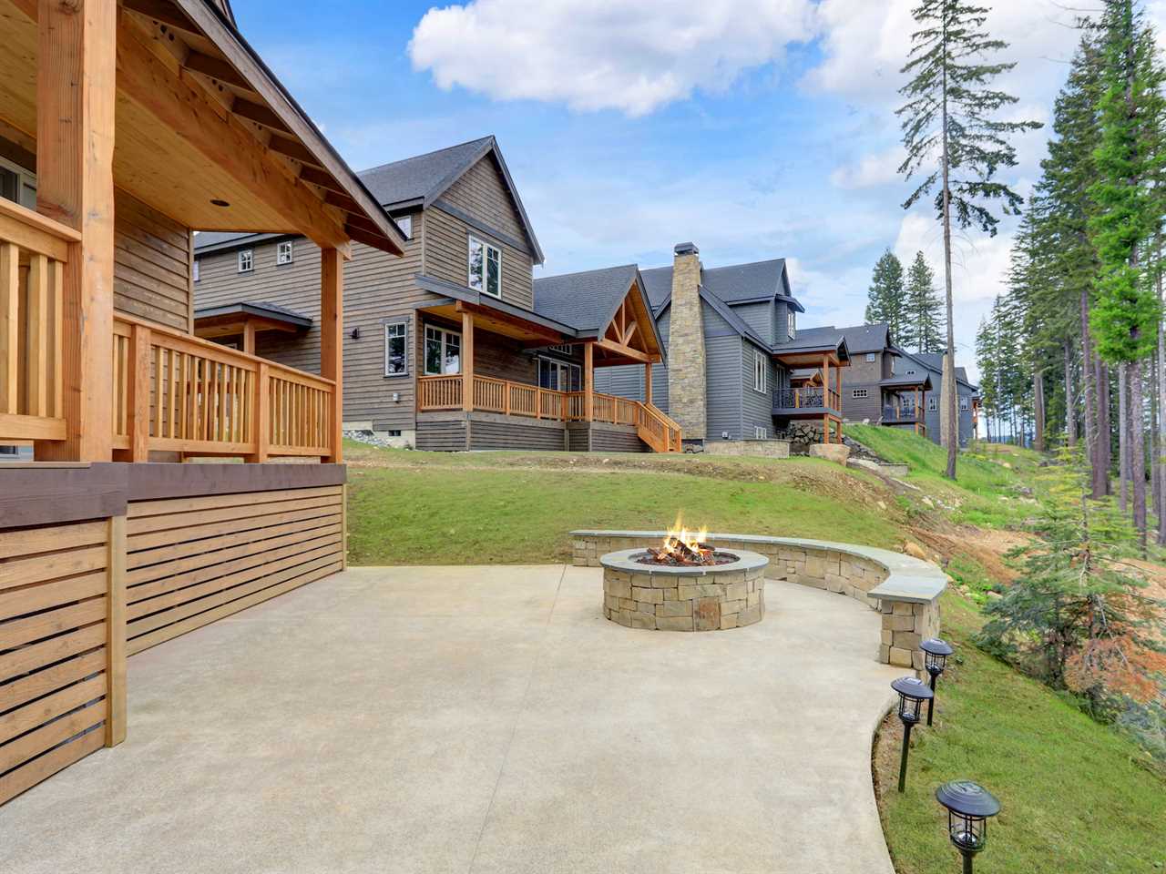 Beautiful wooden back porch with chairs on the hill and large backyard patio with fire pit and pine trees.