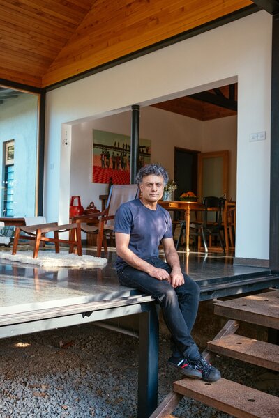 Naeem perches on the black terrazzo floor of the addition. The steel-frame pavilion has custom tracks for sliding walls and doors and is tacked onto the existing 1950s wood-and-masonry building. A narrow deck abuts the extension; stairs lead down to the garden.