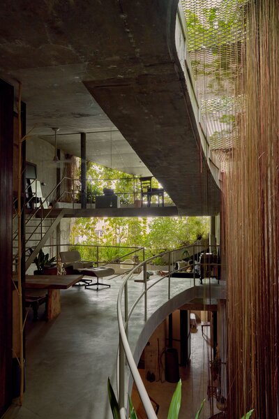 Large cutouts take the place of glass windows and entire walls, inviting sunlight, breezes, and even rain to enter. The roots of a princess vine drop from the roof garden to the ground floor.