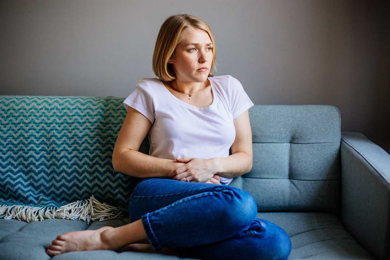 woman with stomach pain sitting on couch.