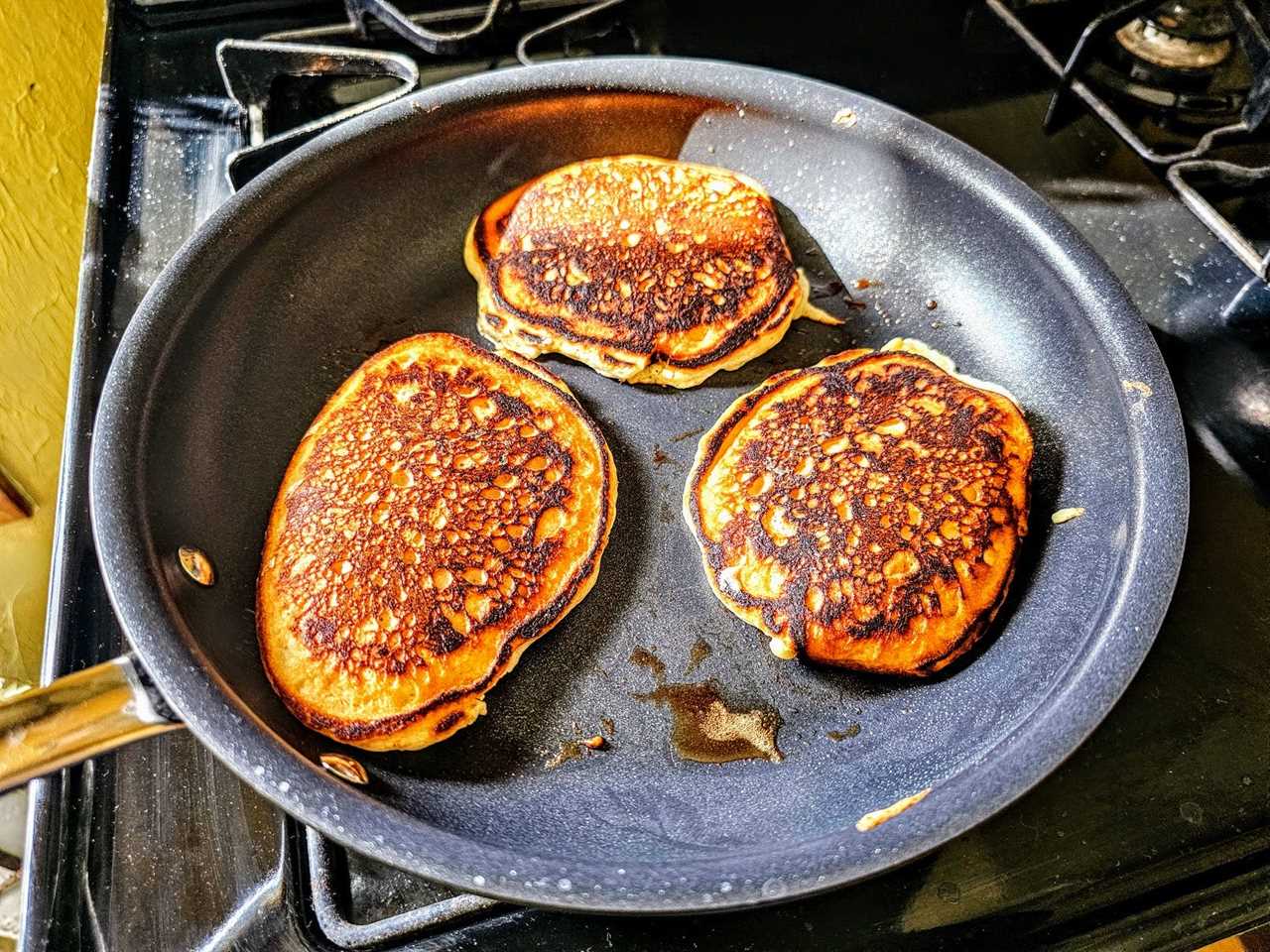 Pancakes are show in a fry pan on a stove.