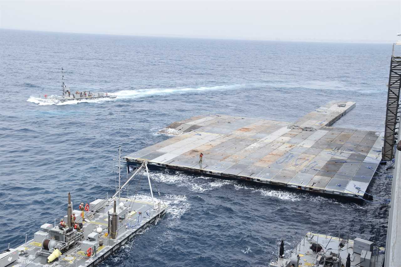 Two boats sail nearby a large metal platform in the sea