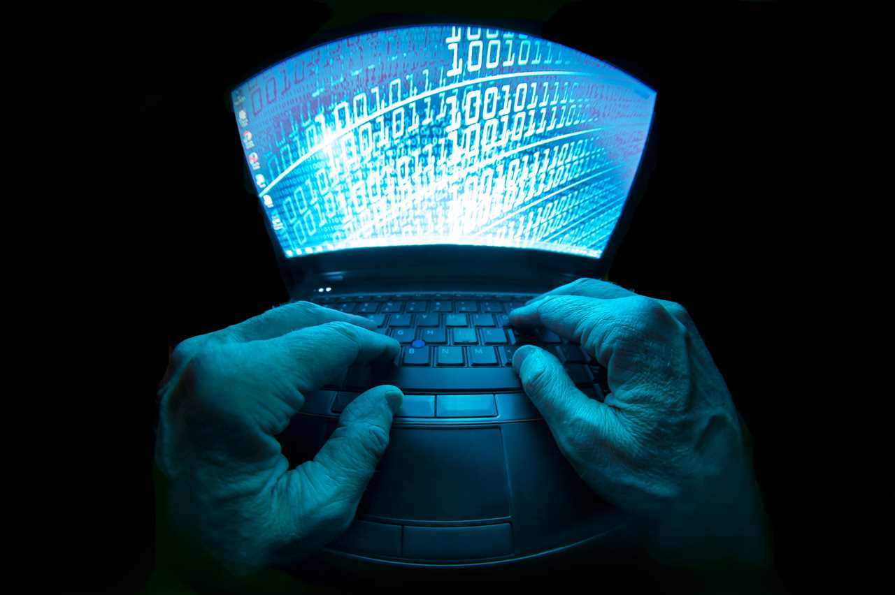 A fisheye view of a pair of a hands typing on a laptop computer, which id displaying a binary code wallpaper