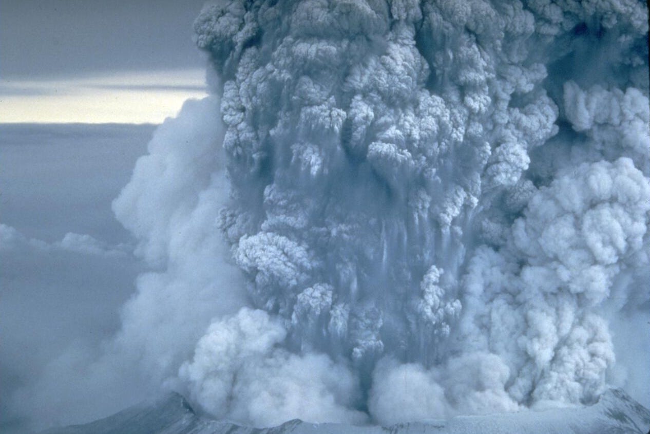 A plume of gray-white ash pouring upward from a volcano