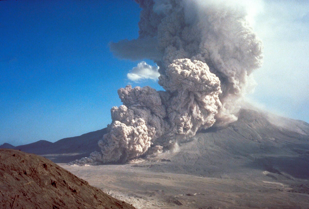 A pyroclastic flow of gas and debris pouring out of Mount St. Helens in a large brownish-white cloud